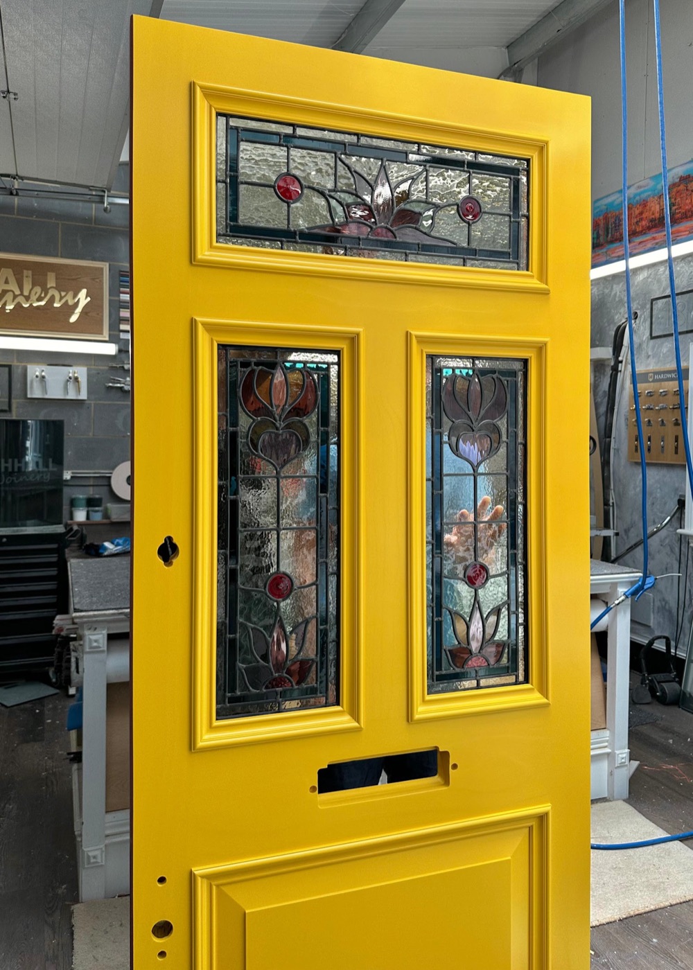 A bright yellow bespoke front door made by Beechhall Joinery with three floral stained-glass panels, standing in the workshop.